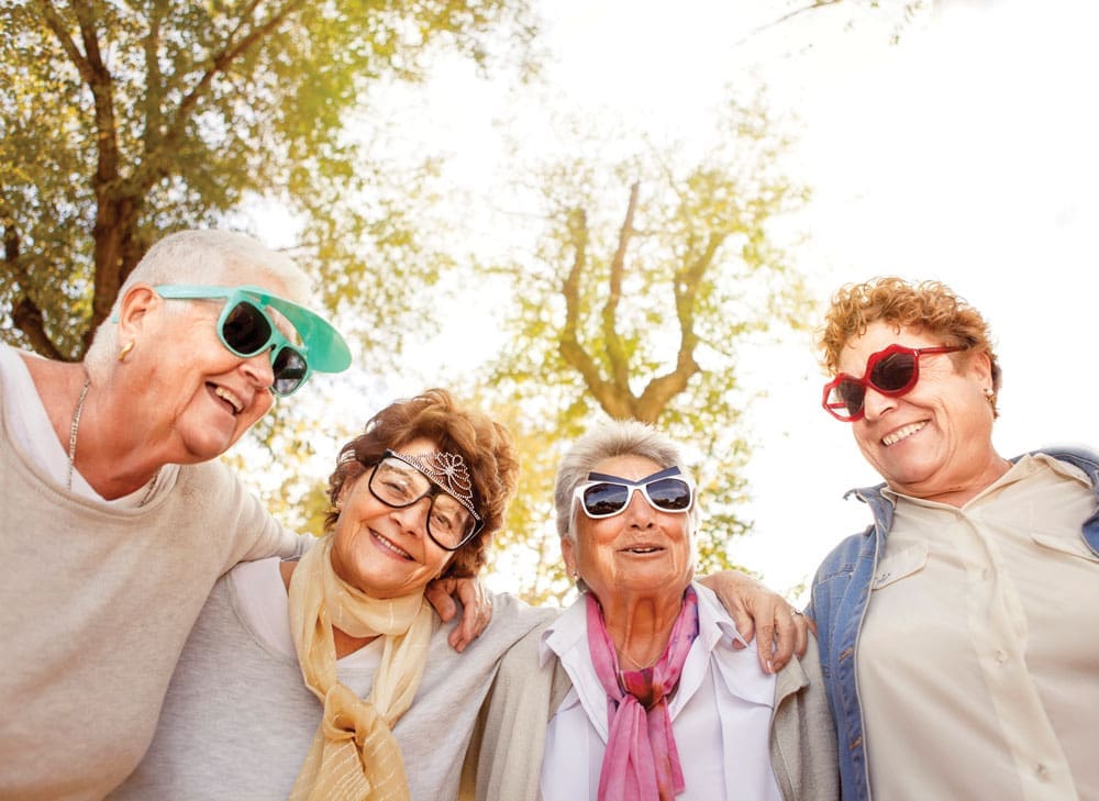 Four older women pose close together in funny sunglasses outdoors 